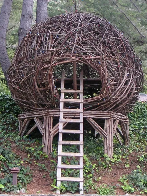 A woven nest sculpture with a ladder among trees at Esalen